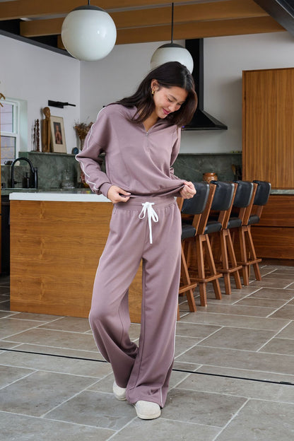 Woman in Thread and Supply Mocha Wide Leg Drawstring Pants stands in a modern kitchen, looking down and smiling.