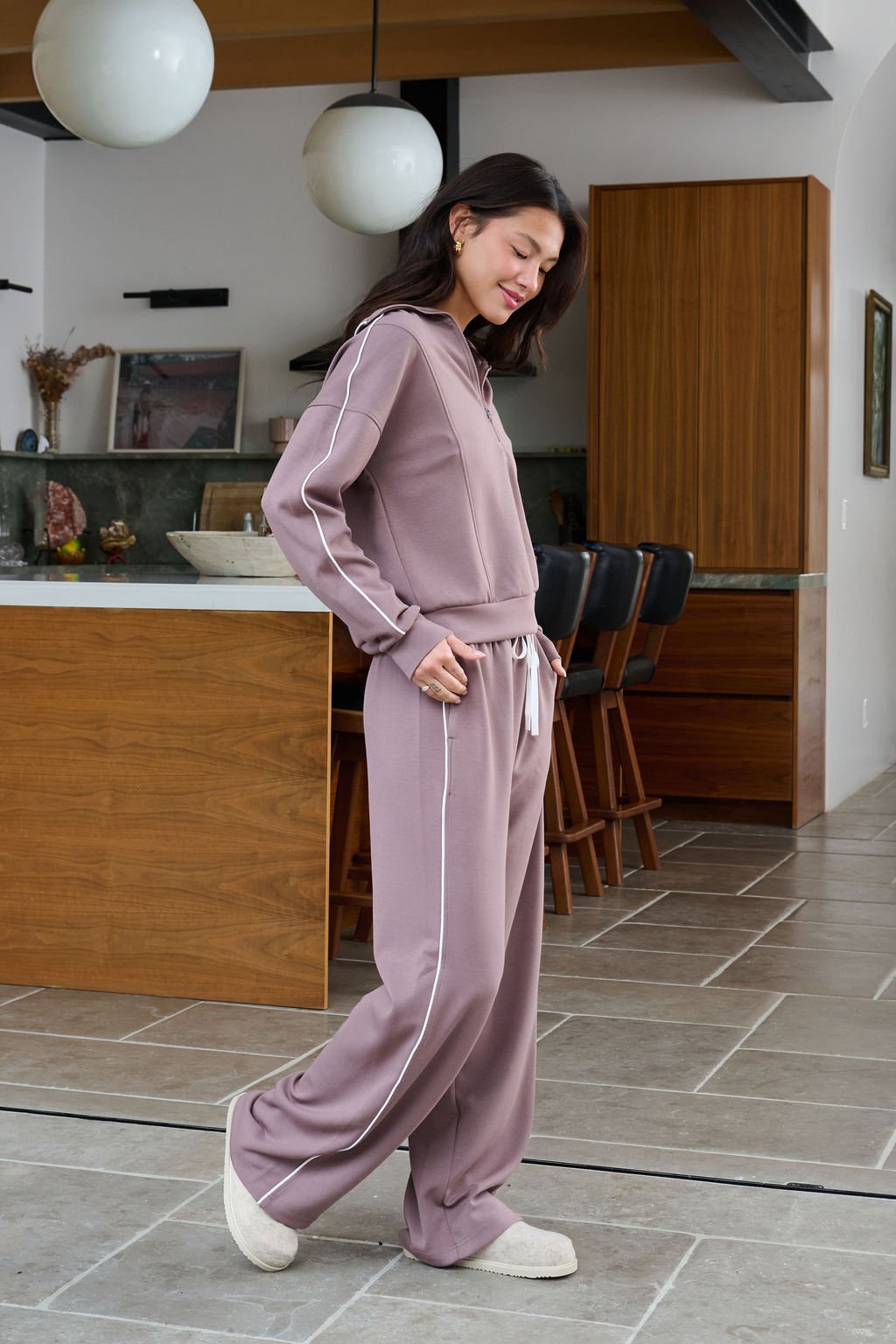 Woman wearing Thread and Supply Mocha Wide Leg Drawstring Pants stands sideways in a modern kitchen, smiling with eyes closed.