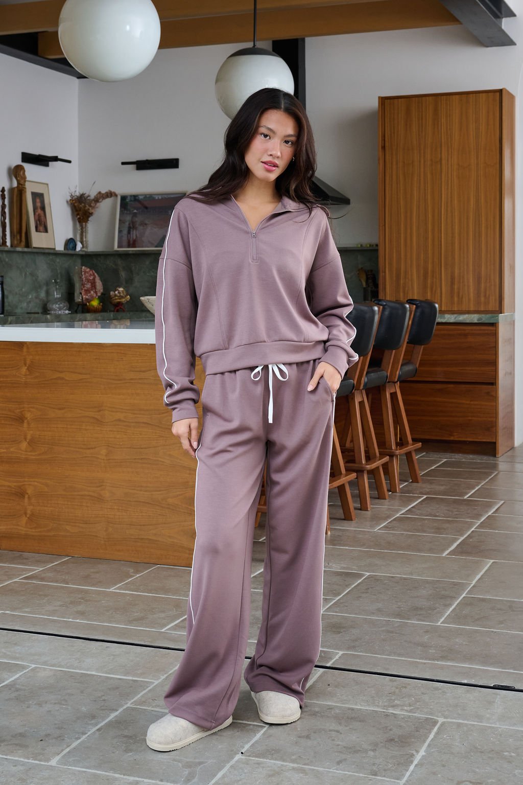 Woman in a modern kitchen wears Thread and Supply Mocha Wide Leg Drawstring Pants, posing with one hand in her pocket.