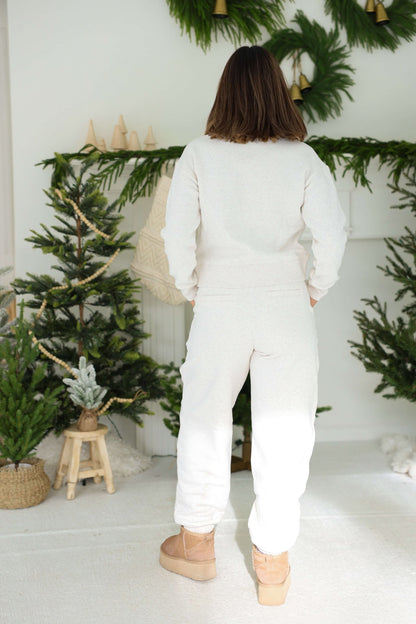 Someone in Thread and Supply Oatmeal Fleece Joggers stands facing away, cozy indoors among small Christmas trees.