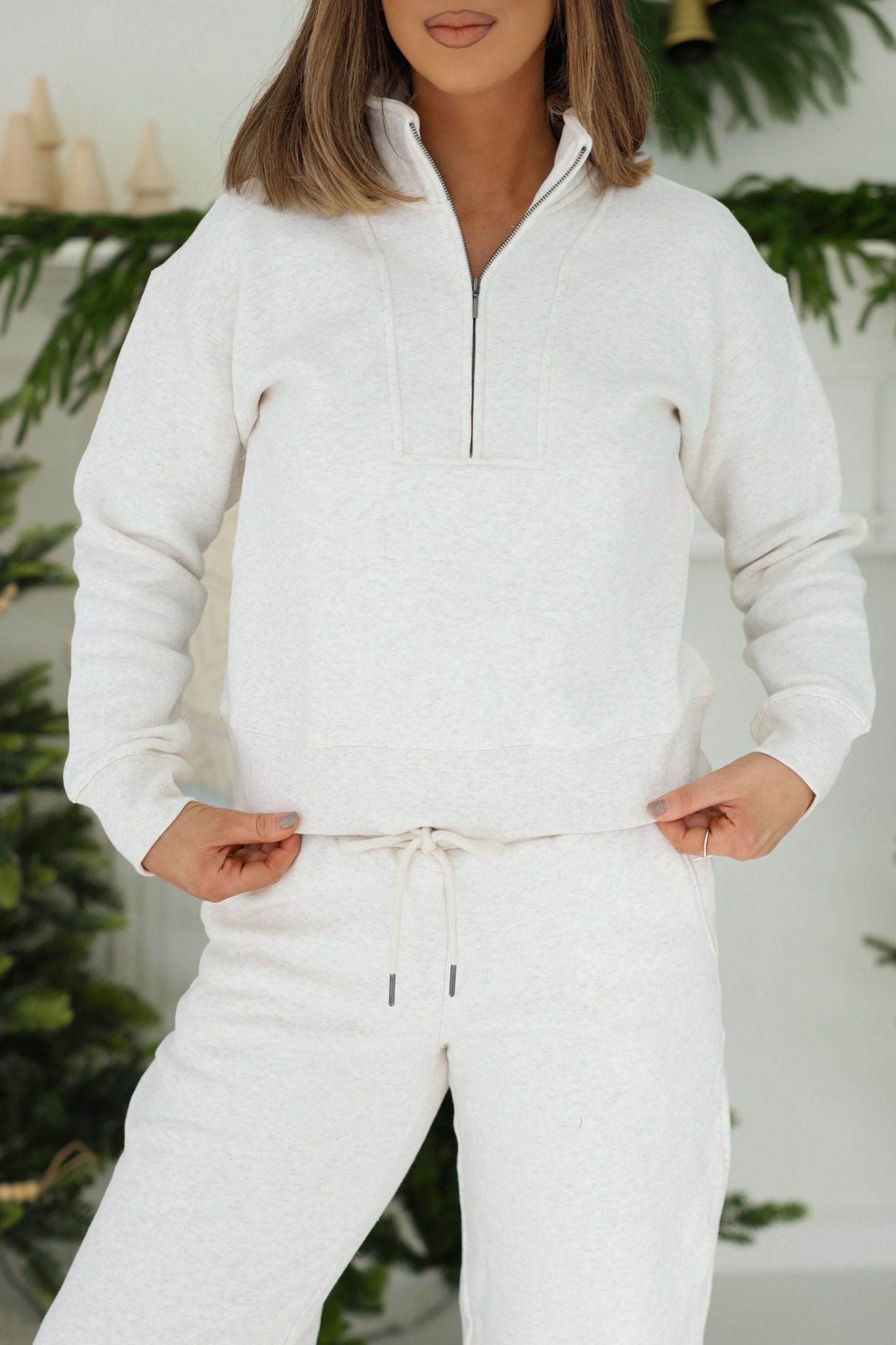 Woman in a Thread and Supply Oatmeal Quarter Zip Sweatshirt stands indoors near plants, paired with matching drawstring pants.