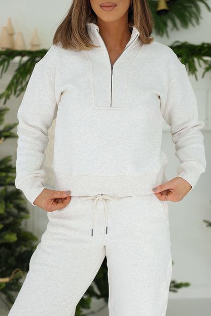 Woman in a Thread and Supply Oatmeal Quarter Zip Sweatshirt stands indoors near plants, paired with matching drawstring pants.