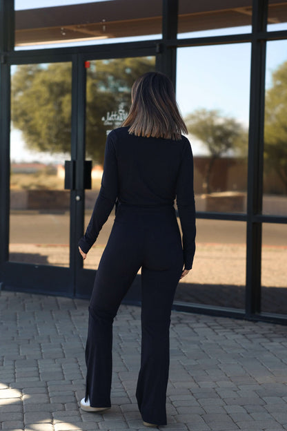 Woman wears Thread and Supply Polina Black Flare Pants, standing outside glass doors, facing away on a sunny day.