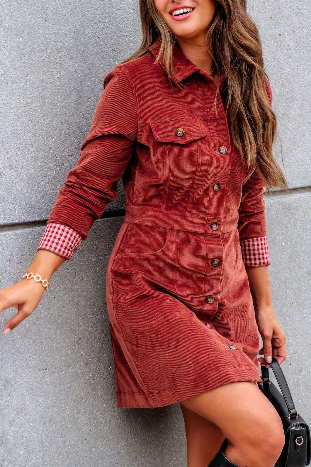 Woman wearing Thread and Supply Rust Corduroy Mini Dress, smiling against a gray wall.