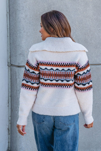 A woman in blue jeans and a Thread and Supply Tan Aztec Bernese Sweater stands with her back to a gray concrete wall.