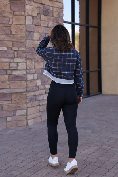 Wearing Thread & Supply Callie Black Leggings, white sneakers, and a plaid jacket, someone walks on a stone path beside a brick wall.