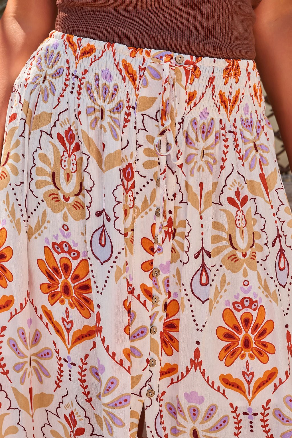 A person wearing a brown top and the Tropical Treasure Print Maxi Skirt - Cream with orange and purple floral patterns.
