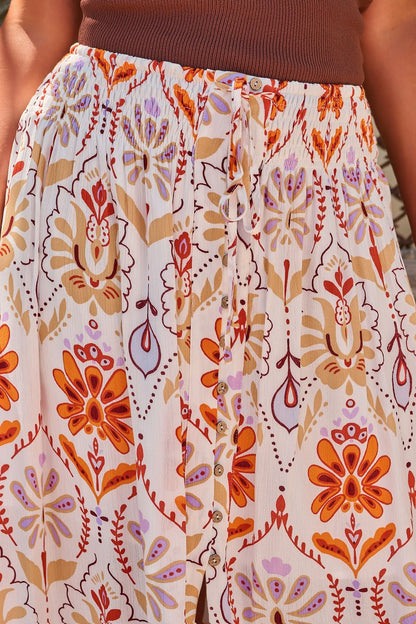 A person wearing a brown top and the Tropical Treasure Print Maxi Skirt - Cream with orange and purple floral patterns.