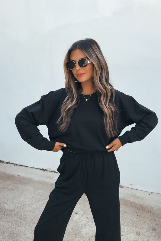 Woman in sunglasses and our Ultra Soft Brushed Fleece Sweatshirt - Black stands confidently, hands on hips, against a light background.