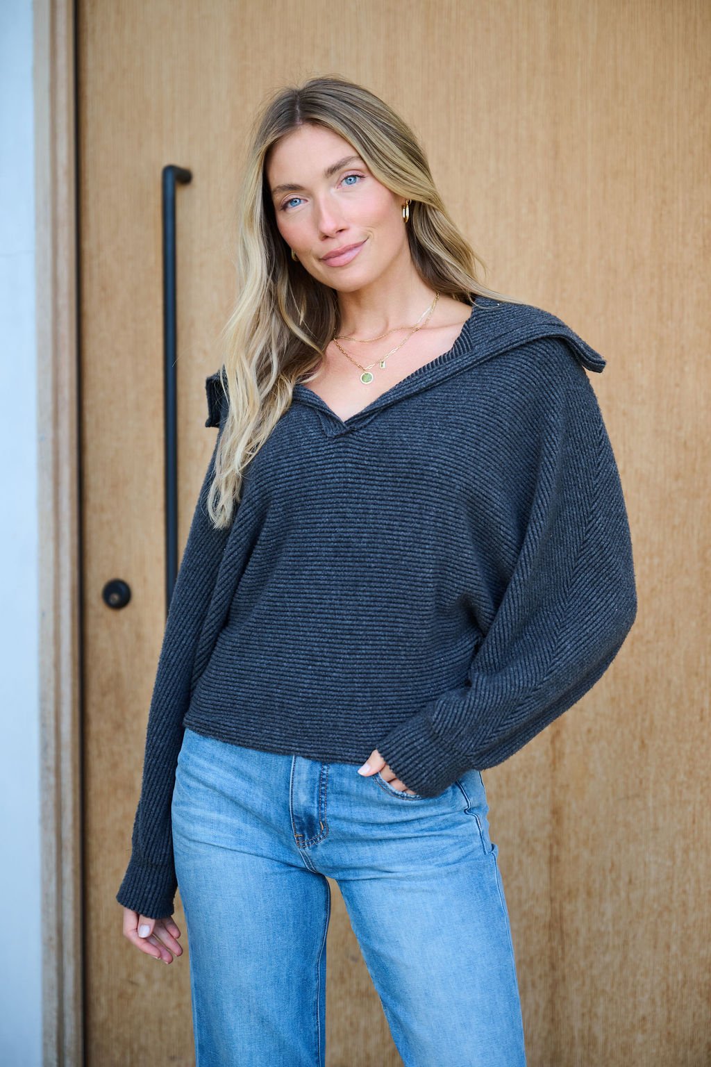 Woman with long blonde hair wears the Ultra Soft Charcoal Collared Pullover, smiling softly in front of a wooden door.