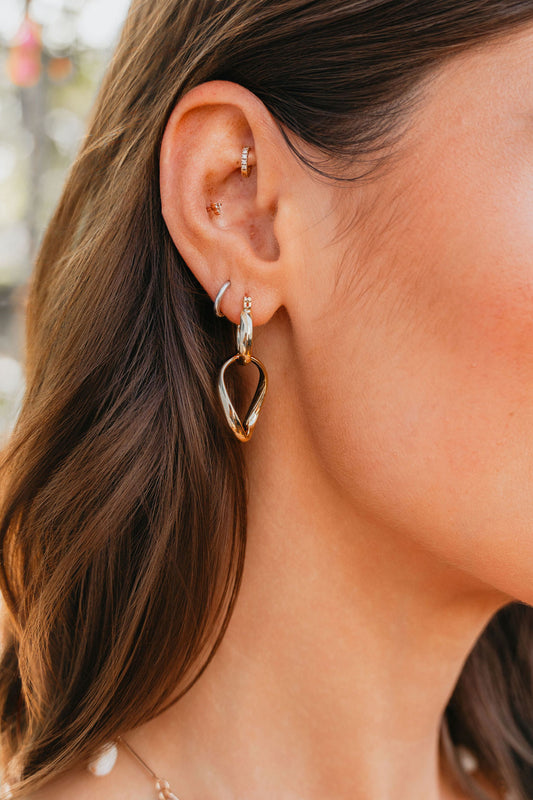 Close-up of a woman's ear with wavy brown hair, wearing Luna Double Hoop Earrings and other gold hoops.