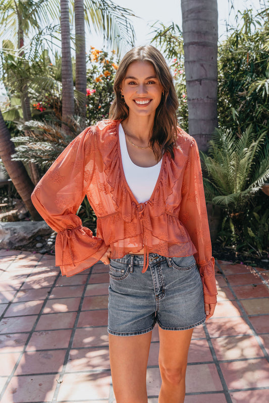A woman smiles outdoors in a Steve Madden Montana Rose Floral Top and denim shorts, surrounded by palm trees on a sunny day.