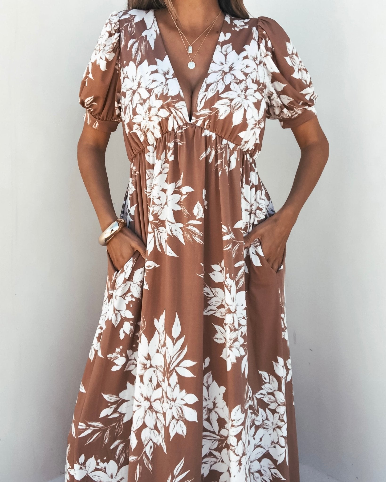 Woman wearing the Valerie Taupe V Neck Print Maxi Dress with pockets, posing against a light wall.