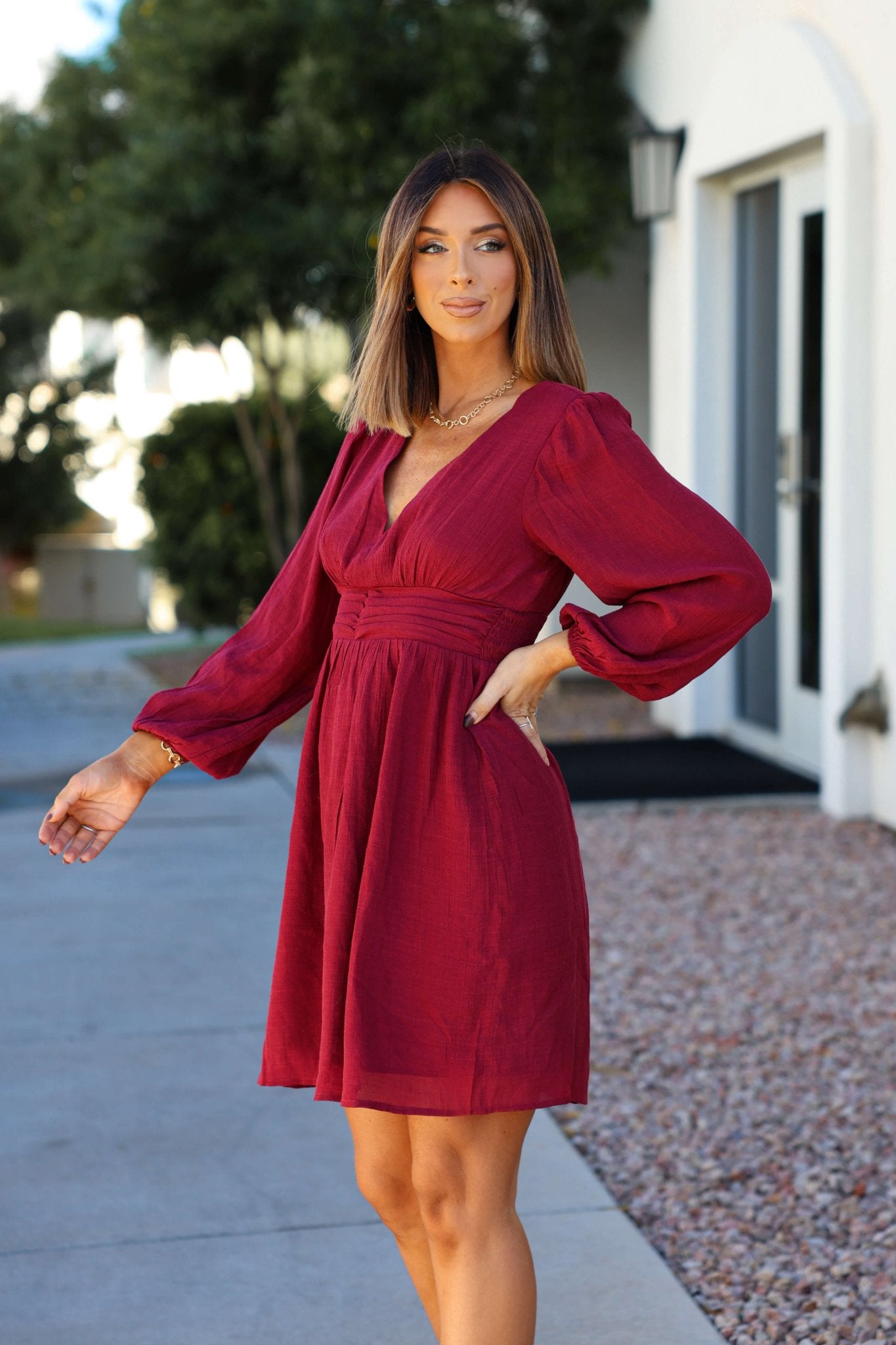 A woman stands outside in the Vanessa Burgundy Ruched Mini Dress, perfect for special occasions.