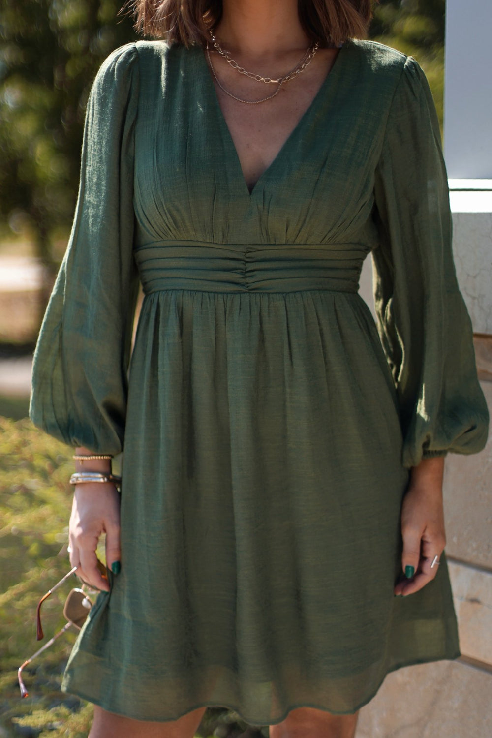 Woman in the Vanessa Green Ruched Mini Dress - FINAL SALE and gold jewelry—ideal for fall weddings or special occasions.