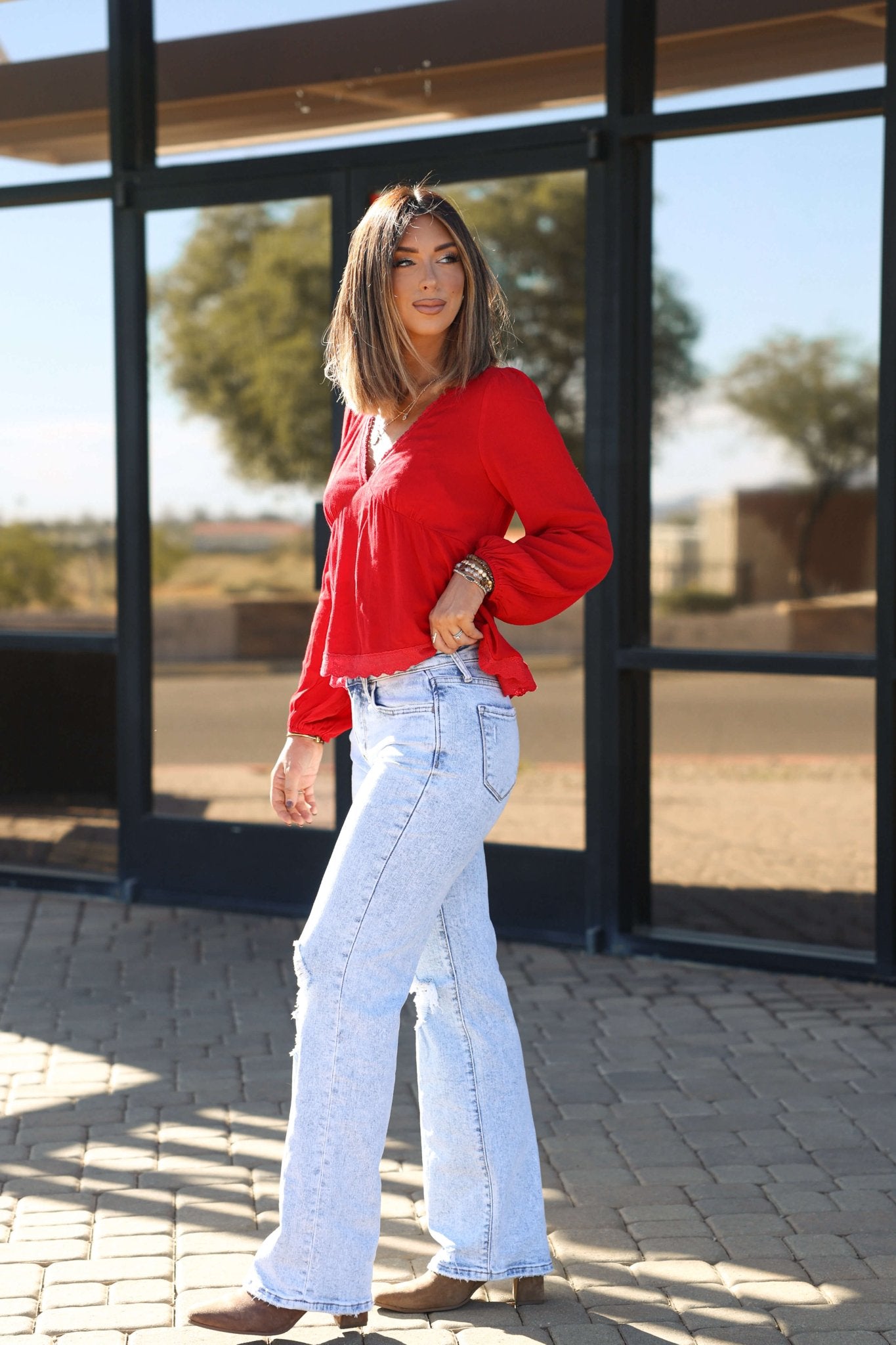 Woman wears Vervet Light Wash Distressed Wide Leg Jeans outside on a stone walkway, with glass windows and trees behind her.