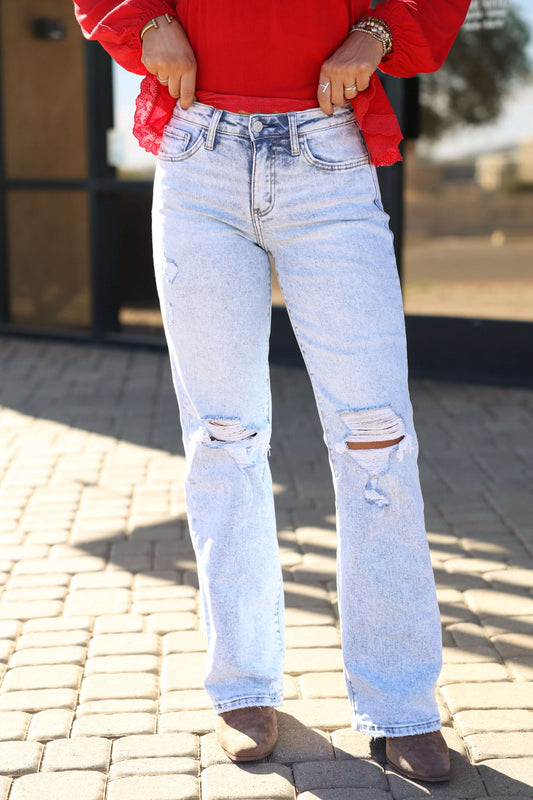 Person wearing Vervet Light Wash Distressed Wide Leg Jeans, a red long-sleeve top, and brown boots on a sunlit paved surface.