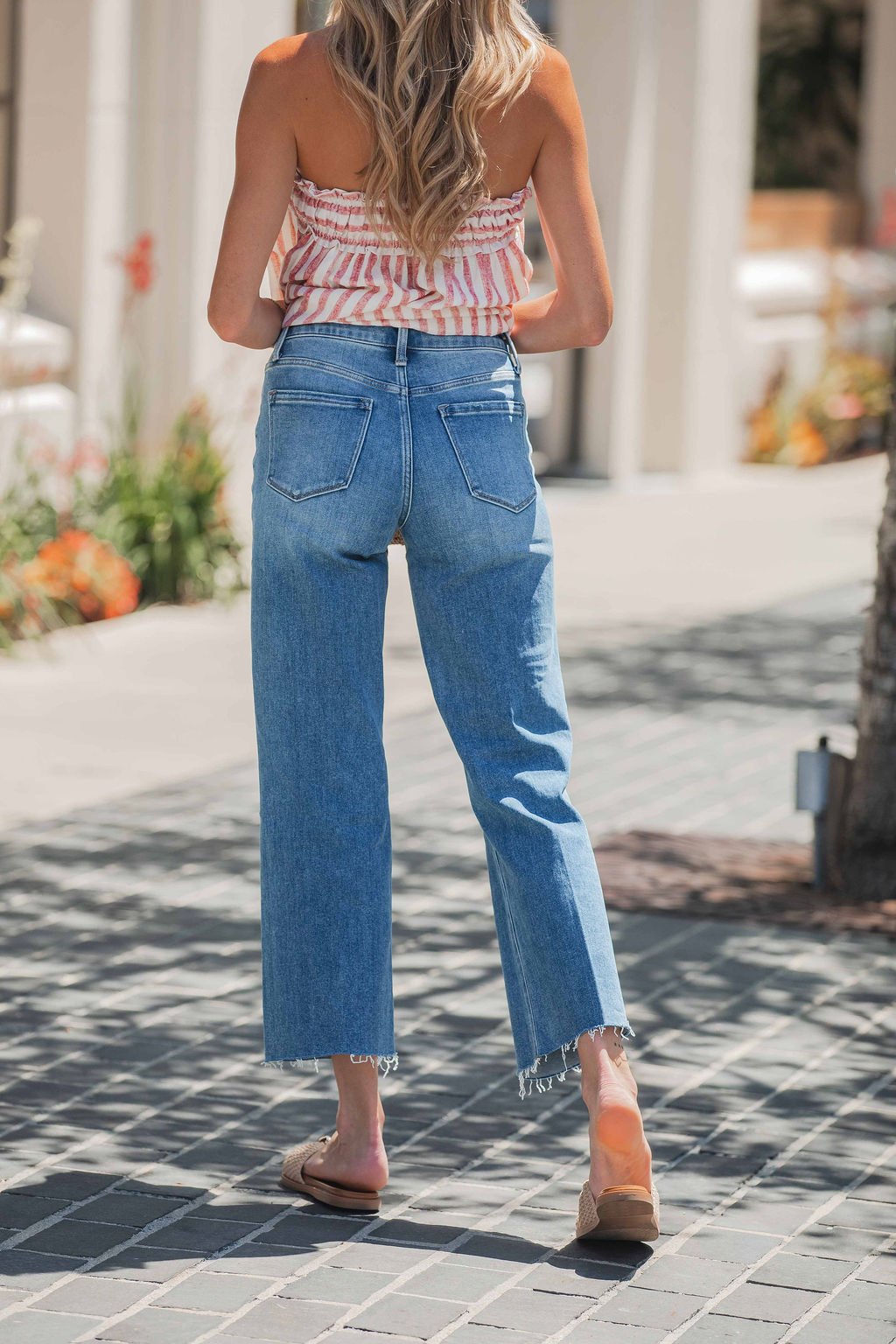 Woman in a striped top and Vervet Raw Hem Distressed Jeans - Medium Wash walks confidently on a sunny sidewalk.