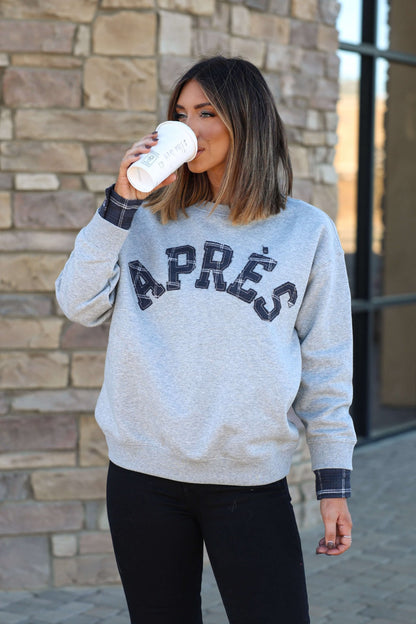 A woman with shoulder-length hair wears a Vintage Havana Grey Apres French Terry Sweatshirt, sipping from a white cup by a brick wall.