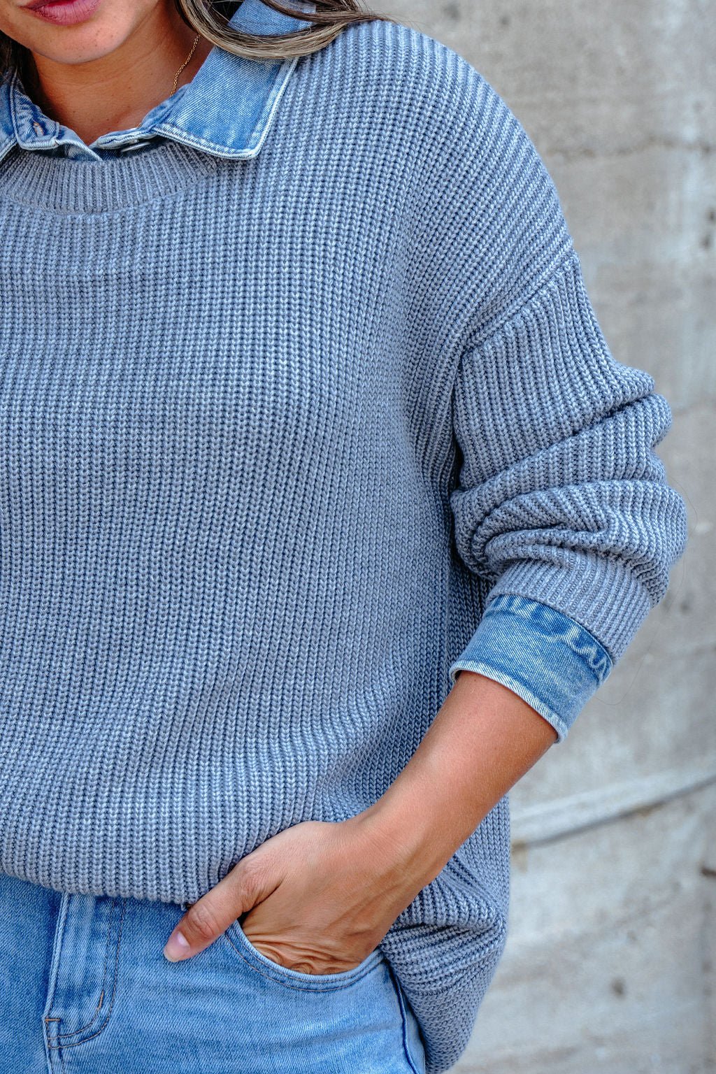 Wearing the Vintage Havana Grey Contrast Ribbed Sweater with denim collar and jeans, hand in pocket by a concrete wall.