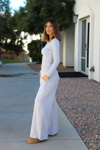 A woman stands outside in a gray top and Vintage Havana Heather Grey Ribbed Flare Pants, with trees and a building behind her.