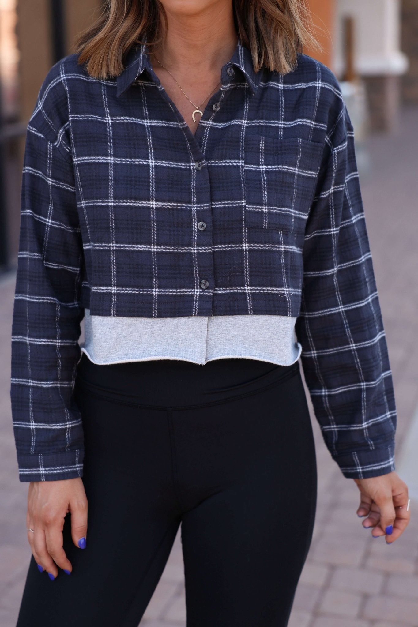 Woman wearing a Vintage Havana Midnight Plaid Flannel Shirt and black leggings, standing outdoors on a paved walkway.
