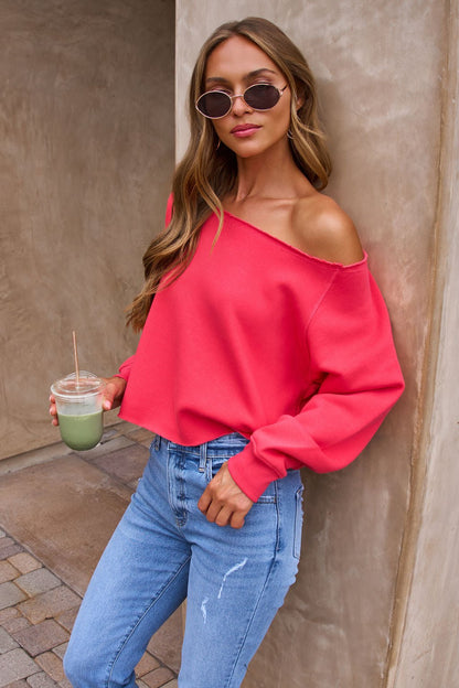 Woman in sunglasses and a bright pink Vintage Havana Off The Shoulder Pullover - Cherry holds a green drink against a tan wall outdoors.