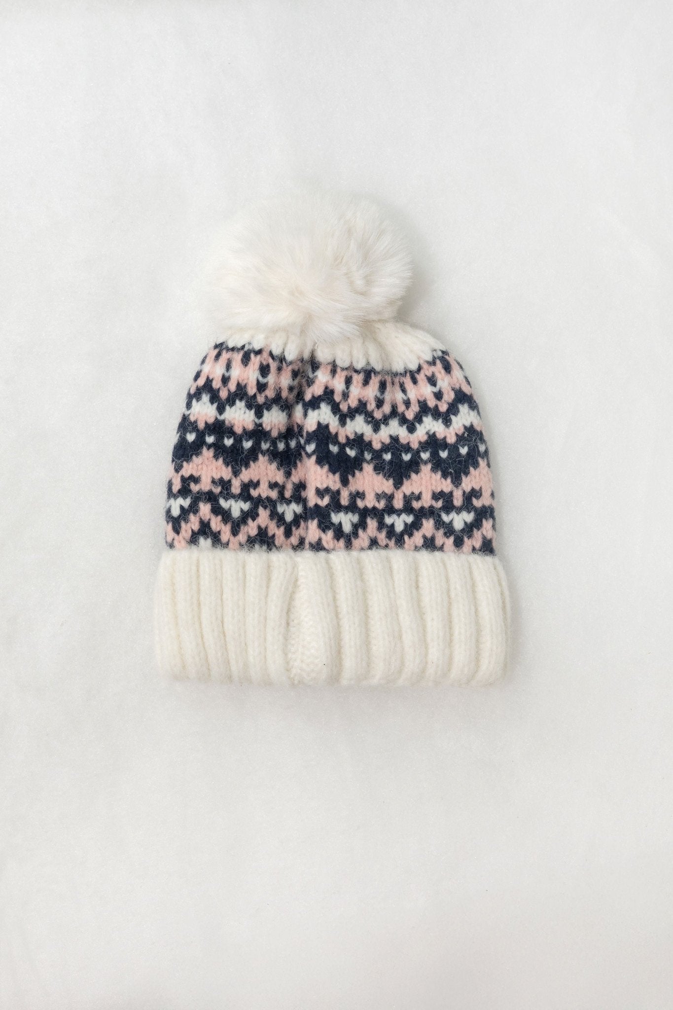 The White Aztec Pom Beanie features a navy and pink pattern, white pom-pom, ribbed knit, and thick brim on a white background.