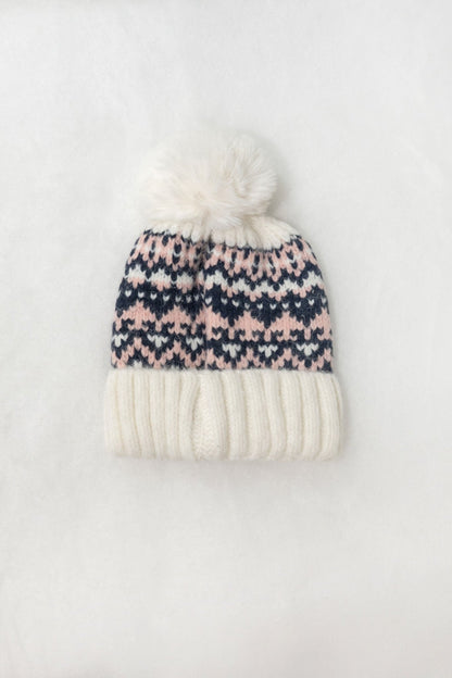 The White Aztec Pom Beanie features a navy and pink pattern, white pom-pom, ribbed knit, and thick brim on a white background.