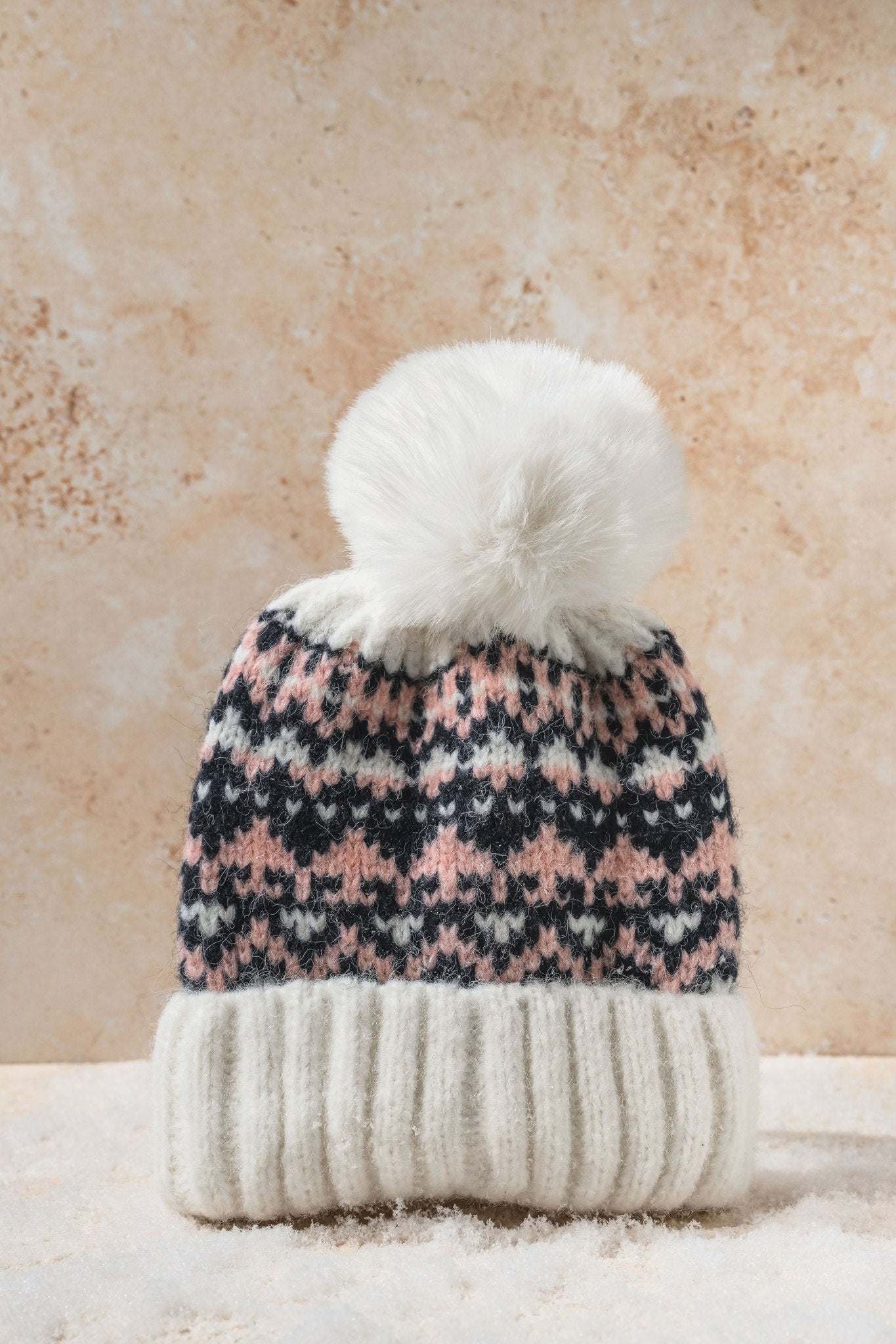 The White Aztec Pom Beanie features a ribbed knit, white cuff, pink and black Aztec pattern, and a fluffy pom-pom.