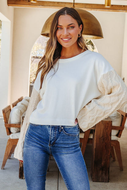 Woman in a White Cable Knit Sweater Sleeve Top - FINAL SALE and blue jeans, smiling indoors.