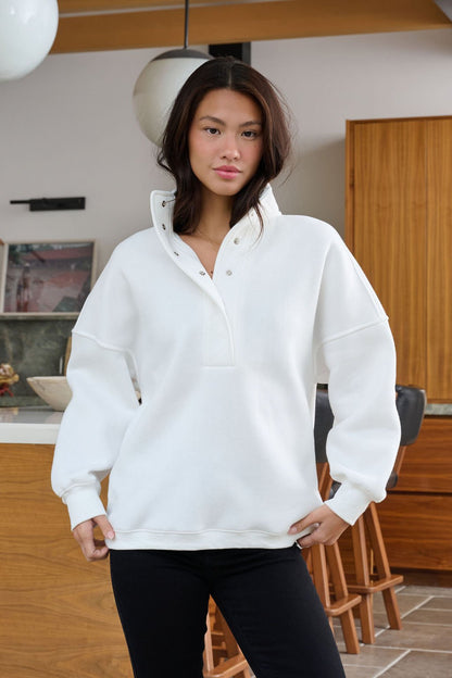 A woman wears a White Collared Button Up Pullover Sweatshirt in a modern kitchen with wooden furniture.