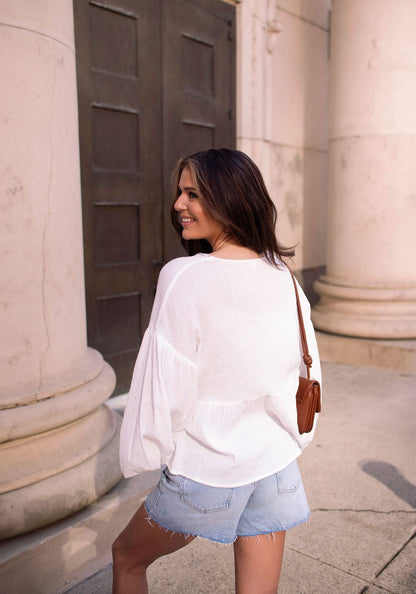 Woman smiles back while strolling near stone columns in a White Flowy Lace Trim Top - FINAL SALE.