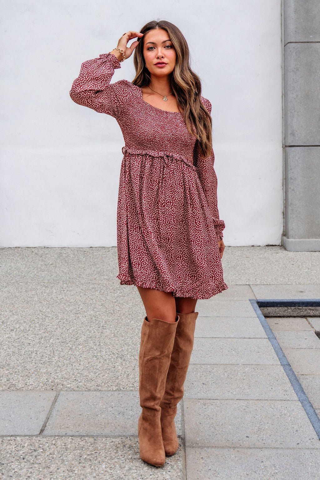 Woman in a Magnolia exclusive Wild Rust Print Smocked Mini Dress - FINAL SALE and tan knee-high boots stands on a sidewalk.
