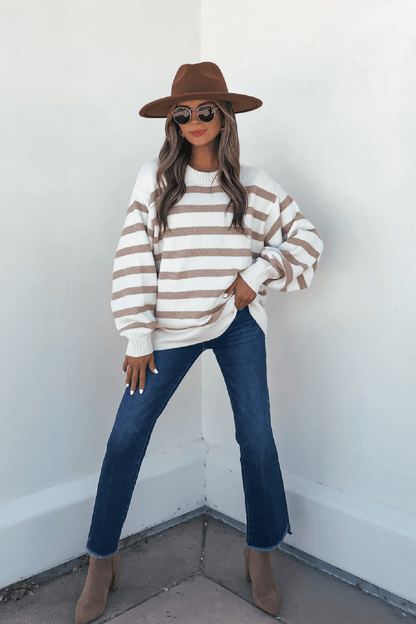 Woman in a brown hat, sunglasses, Willow Cream Stripe Ribbed Sweater, blue jeans, and tan boots stands by a white corner wall.