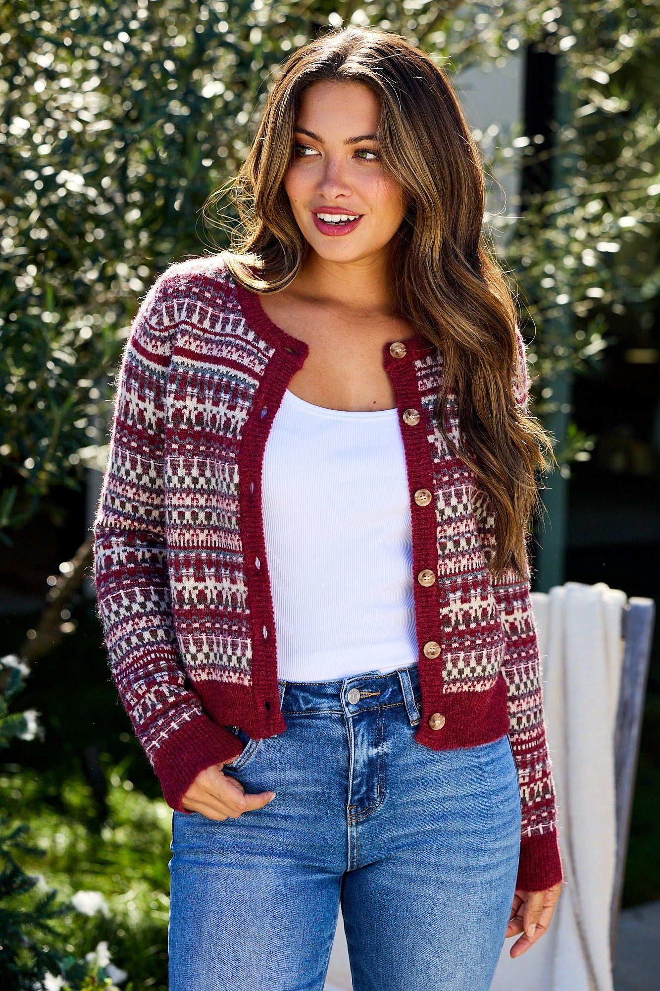 Woman wearing a Wine Fair Isle Button Down Cardigan, white tank top, and blue jeans, smiling outdoors.