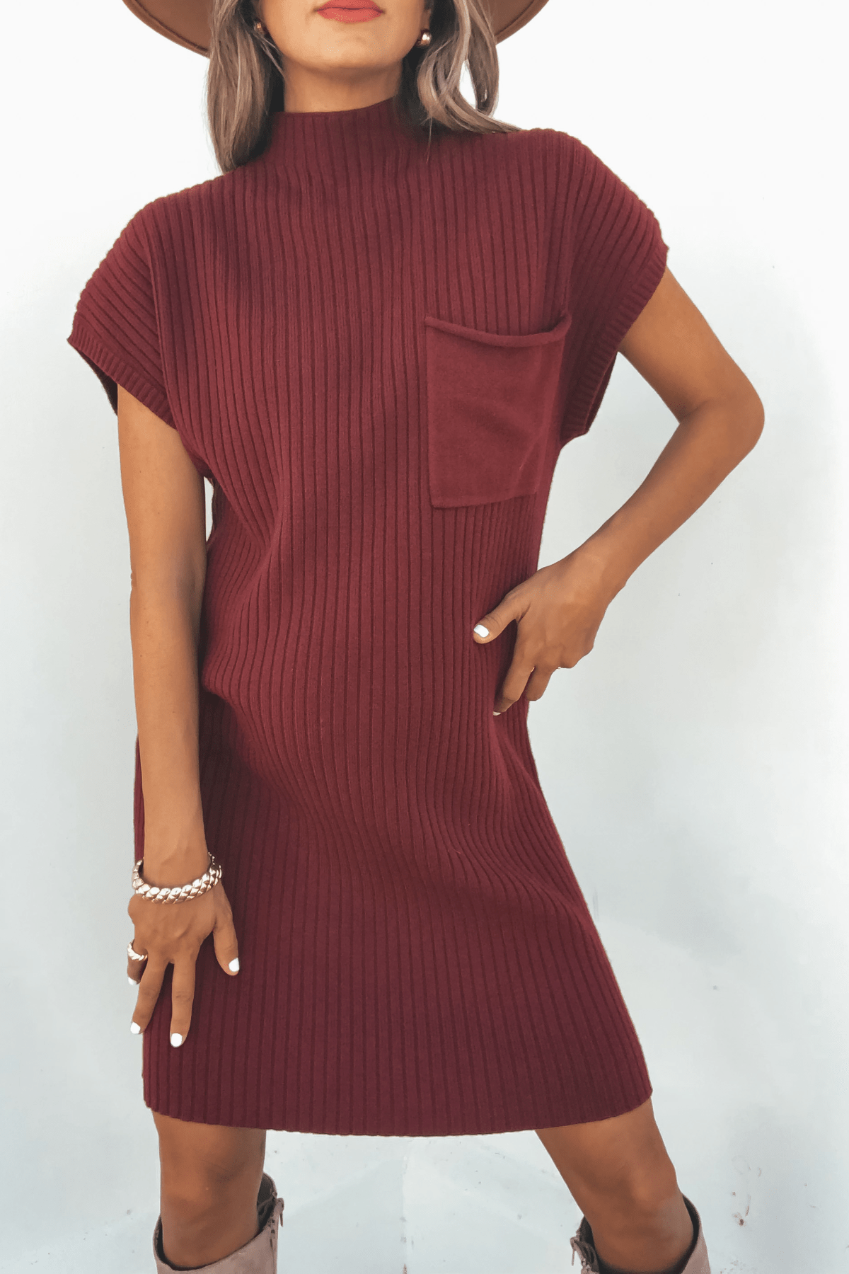 Woman wears Wine Mock Neck Mini Sweater Dress—mini length, ribbed, short sleeves, chest pocket—styled with bracelet and hat.