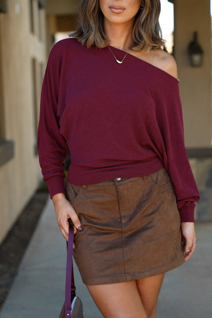 Woman in a Wine Off The Shoulder Crepe Top and brown mini skirt, standing outdoors with a matching purse.