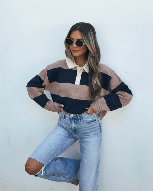 A person wears a Striped Sweater - Mocha And Navy with a white collar and light wash ripped jeans.