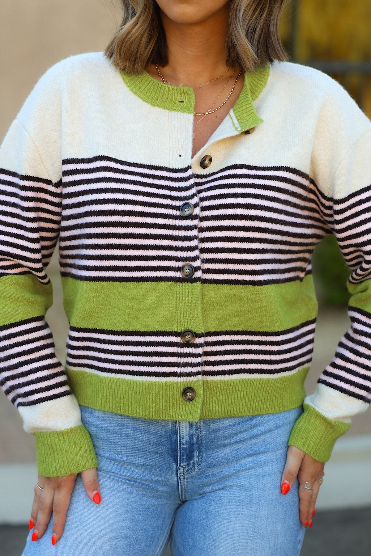 Model wears WISHLIST WL26-13527 Avocado Striped Button Front Cardigan and blue jeans, with visible bright orange nails outdoors.