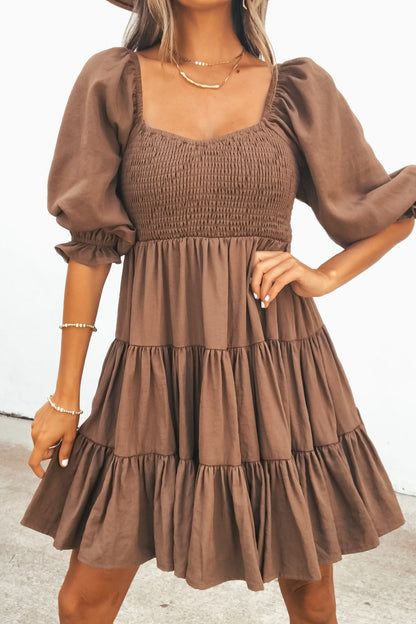 Woman models the Wrenley Tiered Mini Dress in brown, featuring puff sleeves, smocked bodice, and a baby doll silhouette.