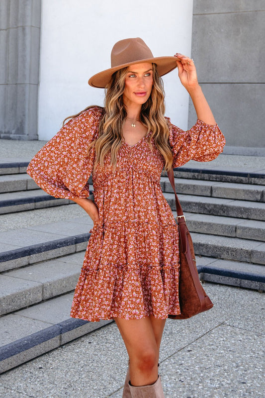 A woman wearing a Floral Mini Dress - Rust with three-quarter sleeves and a wide-brimmed hat.