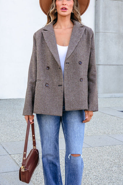 A woman wearing a YURA YJ9036BJ BROWN DOUBLE BREASTED HOUNDSTOOTH BLAZER, white top, and distressed blue jeans, holding a small brown handbag.