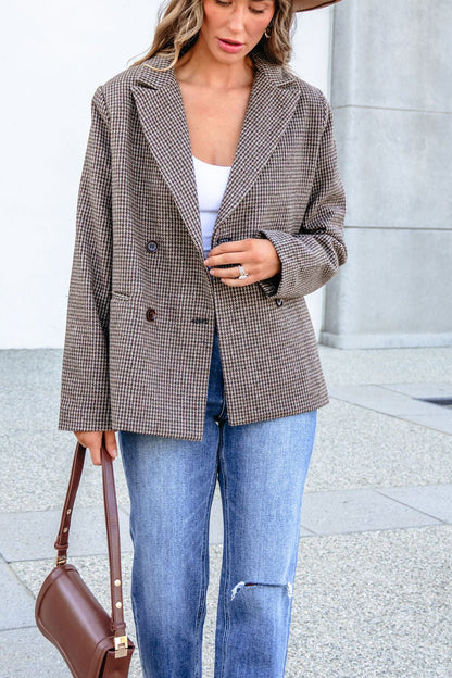 A woman wearing a YURA YJ9036BJ BROWN DOUBLE BREASTED HOUNDSTOOTH BLAZER, white top, and blue jeans, carrying a brown handbag.