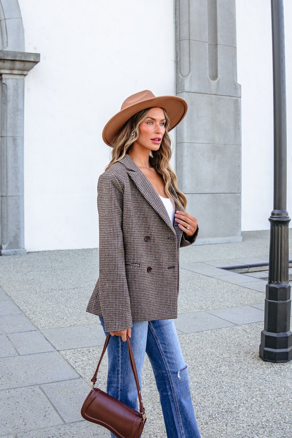 A woman wearing a tan wide-brim hat, a YURA YJ9036BJ BROWN DOUBLE BREASTED HOUNDSTOOTH BLAZER, and blue jeans.