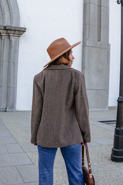 A woman seen from behind, wearing a YURA YJ9036BJ BROWN DOUBLE BREASTED HOUNDSTOOTH BLAZER, blue jeans, and a wide-brimmed hat.
