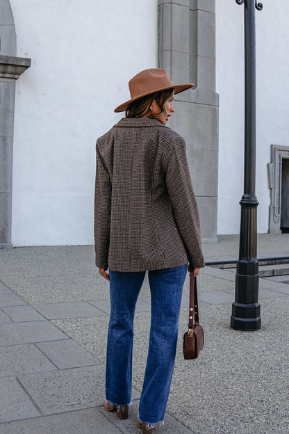 A woman seen from behind, wearing a brown fedora, a YURA YJ9036BJ BROWN DOUBLE BREASTED HOUNDSTOOTH BLAZER, and blue jeans with a shoulder bag.