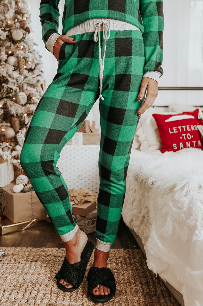 Person in the Christmas Morning Green Plaid Pajama Set stands by a holiday tree and a Letters to Santa pillow.