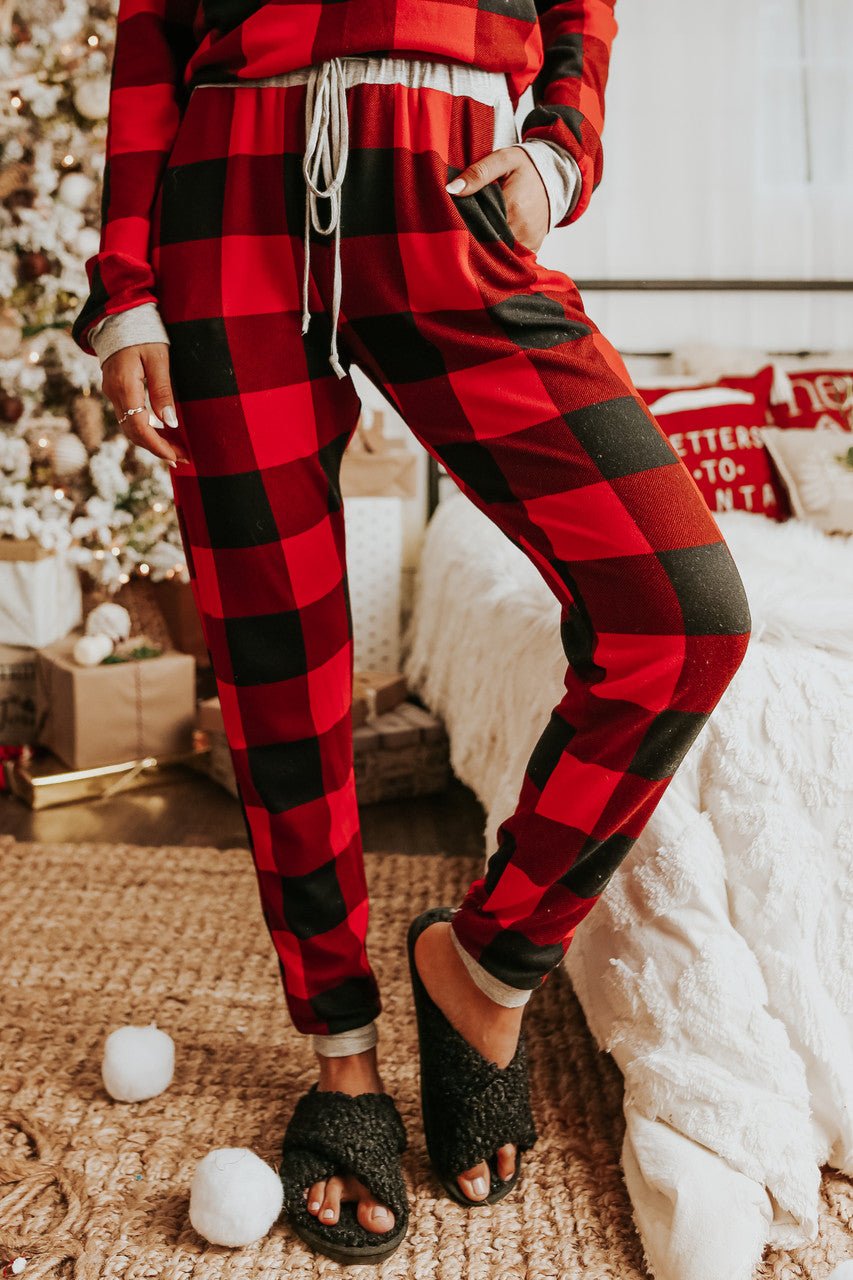 Wearing the Christmas Morning Red Plaid Pajama Set, this person stands by a festively decorated bed and Christmas tree.