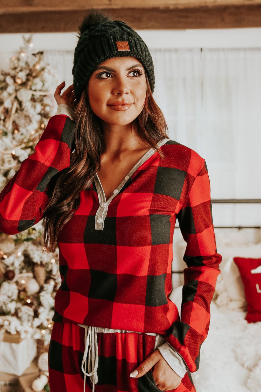 Woman in the Christmas Morning Red Plaid Pajama Set stands indoors by a decorated Christmas tree, smiling softly.